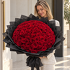 Model holding 100 fresh roses hand-tied bouquet with black wrapping paper