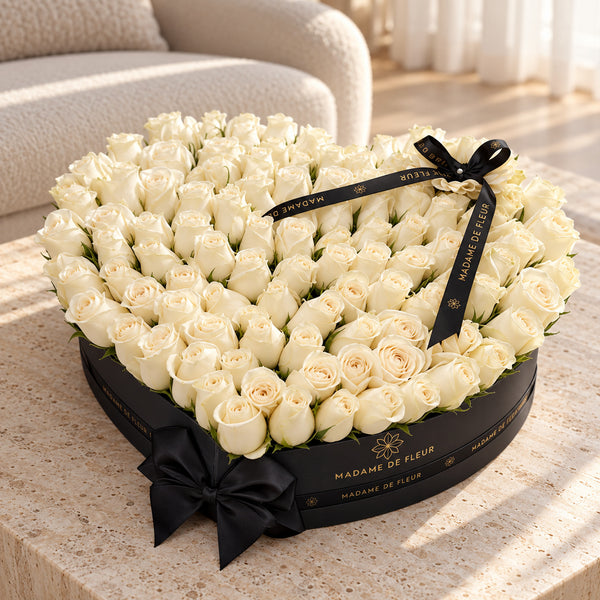White fresh roses in a black heart-shaped Madame de Fleur box on a sunlit stone table