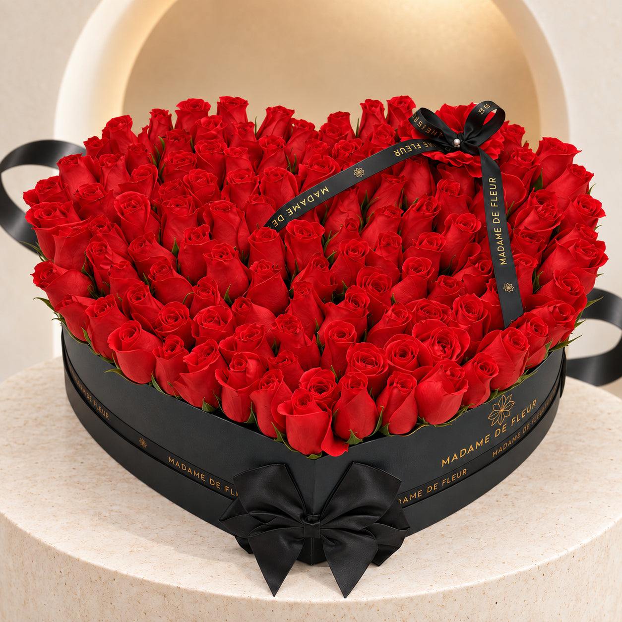 Red fresh roses in a black heart-shaped Madame de Fleur box with black satin ribbon, against an ivory arch