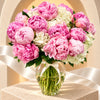 Blushing Embrace peonies and hydrangeas in a tall glass vase against the Madame de Fleur arch background with a white ribbon